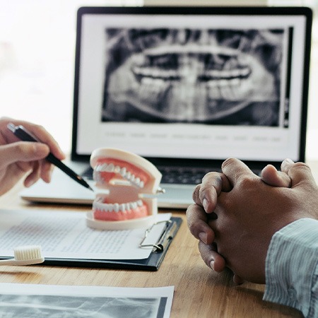 Dentist’s and patient’s hands at desk with X-rays, model teeth, and treatment plan