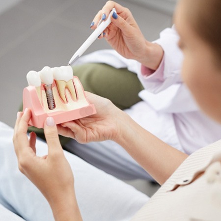 : A young woman holding a dental implant model while a dentist explains treatment