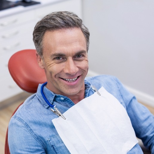 Older man in denim shirt smiling in dental chair