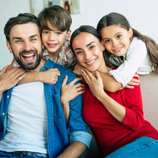 Parents and two young children smiling while sitting on living room couch