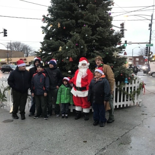 Dentist dressed up as Santa standing in front of Christmas tree on sidewalk