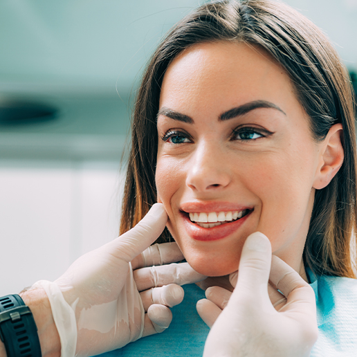 Gloved hands touching the face of a smiling woman in dental chair