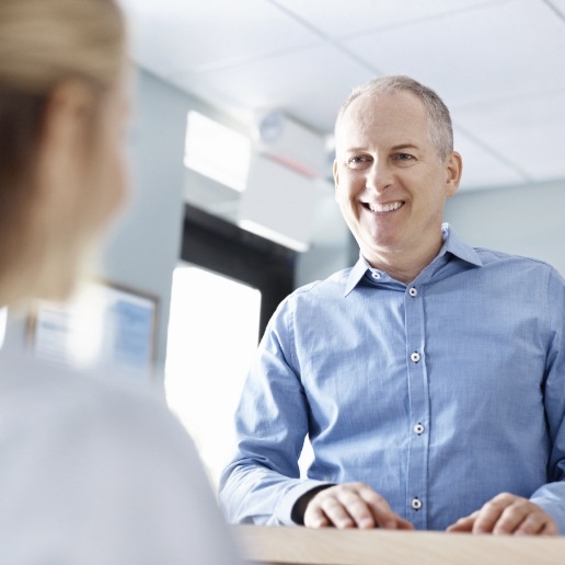 Man in light blue shirt talking to person at dental office front desk