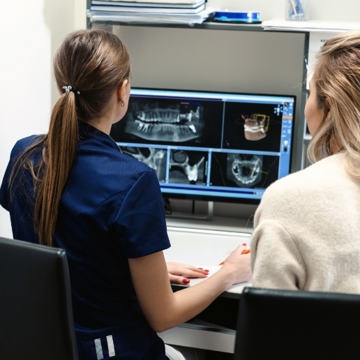 Dental team member and patient looking at digital dental x rays on computer screen