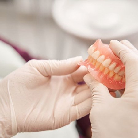 Gloved hands holding full set of dentures