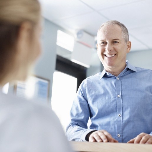 Man in light blue shirt talking to person at dental office front desk