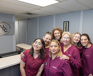 Several smiling dental team members gathered around front desk in Hammond dental office