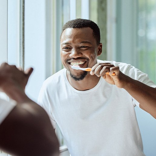 Man smiling while brushing his teeth in bathroom