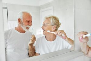 Happy older couple brushing their teeth in front of bathroom mirror